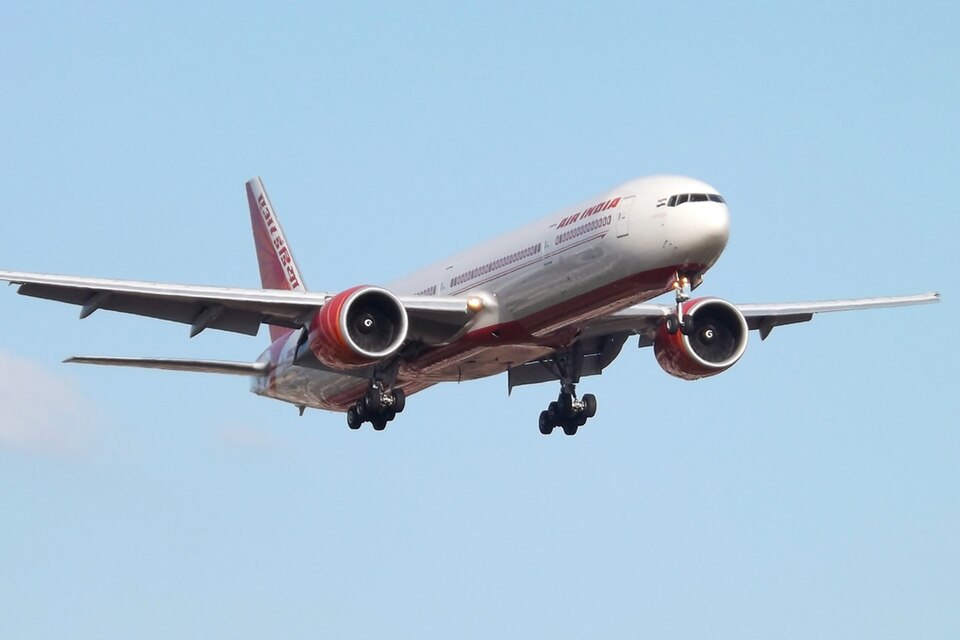 Air India's Boeing 777 is taking off on a sunny day, and the sky is very light blue. The aircraft's landing gear is out.