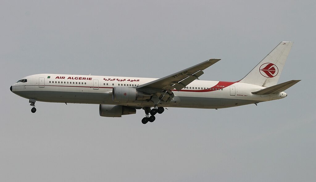 Air Algerie Boeing 767 flying through the grey sky. Landing gear is out. White and red livery, with symbol on the tail of the aircraft.