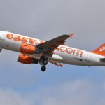 An easyJet aircraft flying towards the left side of the frame. White and orange livery. Blue sky and clouds in the background.