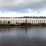 Large BAE Systems industrial building beside a river under cloudy skies, with the company logo visible on the exterior.