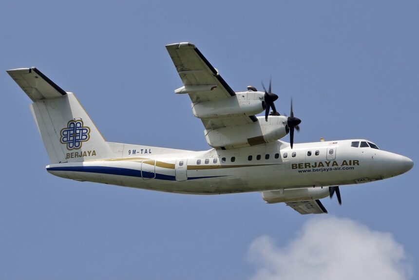 Berjaya Air small jet flying over blue sky; some clouds are visible.