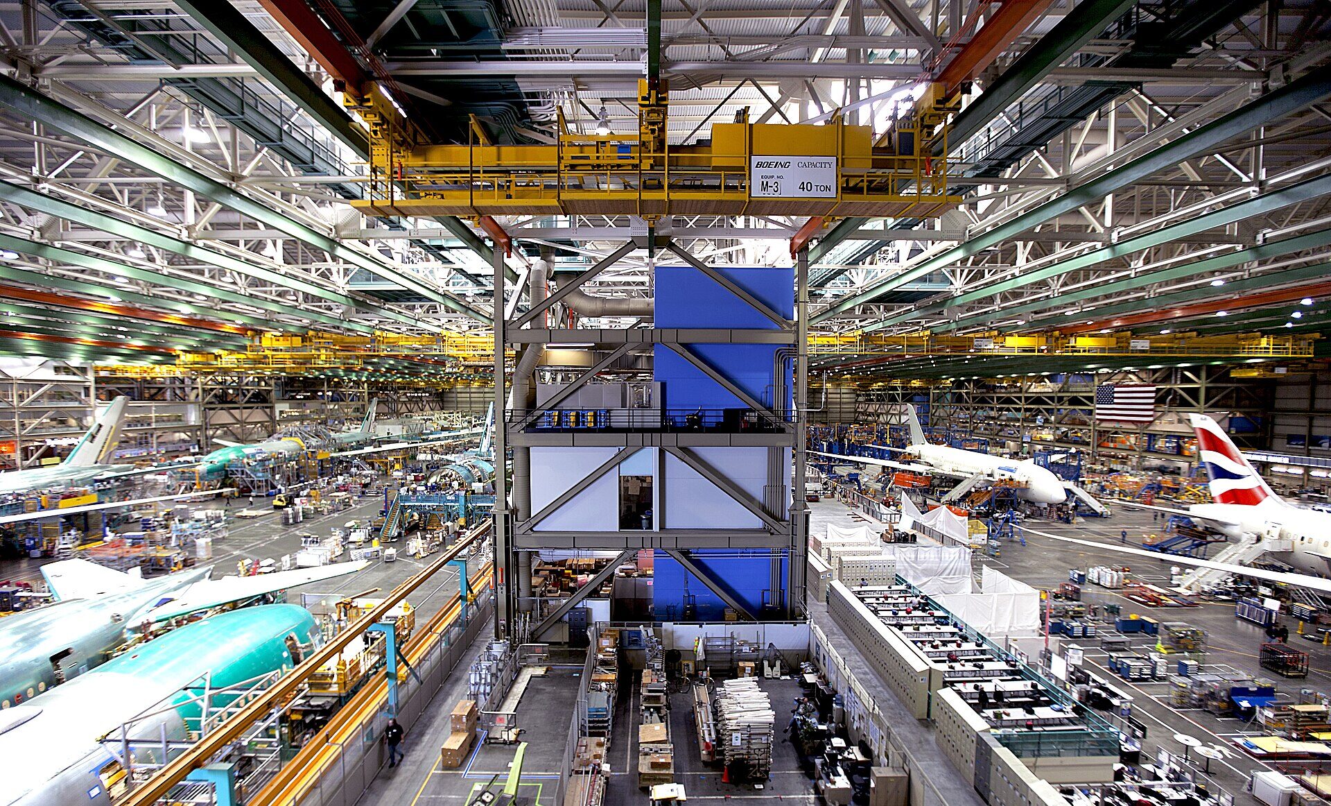 Interior of the Boeing Everett factory showing large aircraft assembly areas with machinery, tools, and partially assembled plane components across the production floor