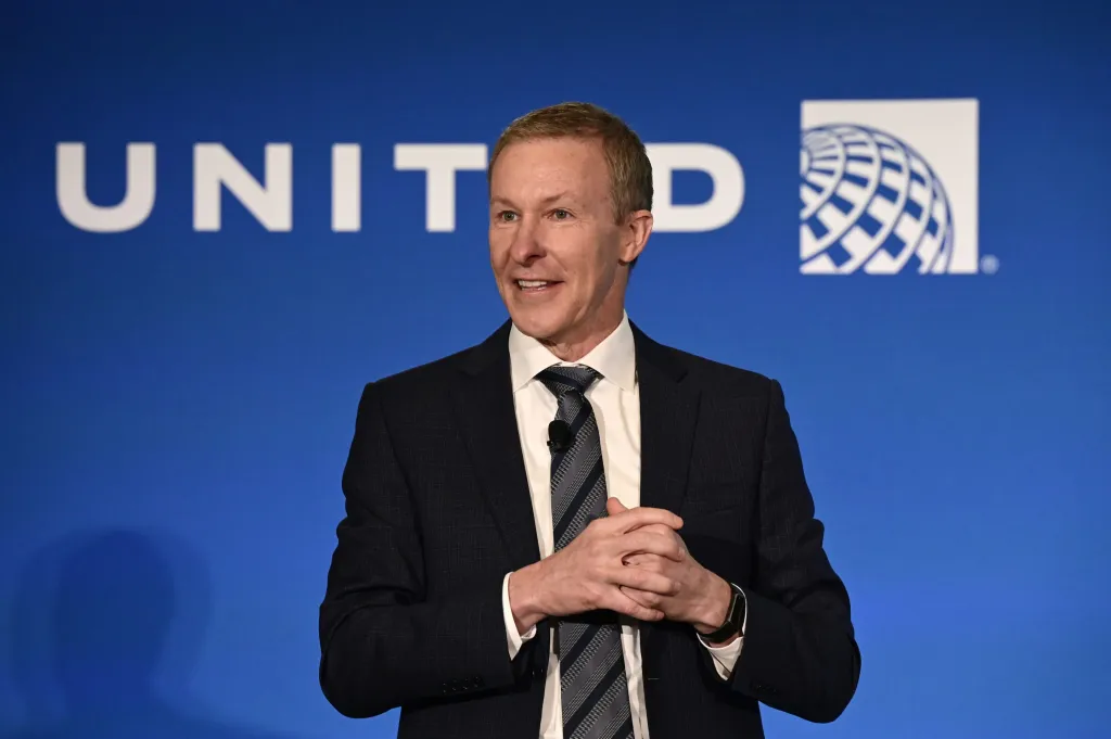 Medium close-up of Scott Kirby, the CEO of United Airlines, standing in front of a blue panel 