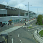 Edinburgh Airport terminal building with drop-off lanes, pedestrians, and transport access outside the entrance.