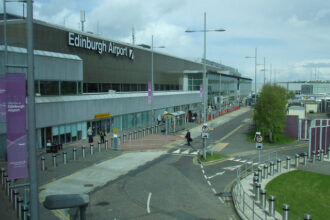 Edinburgh Airport terminal building with drop-off lanes, pedestrians, and transport access outside the entrance.
