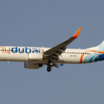 A Flydubai B737 with a white, blue and orange livery flying under a blue sky.