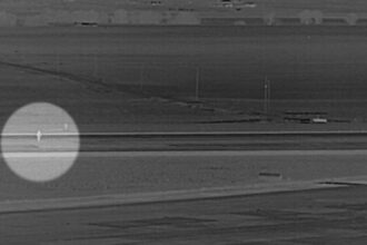 Grayscale surveillance-style image from Denver International Airport showing a man highlighted with a circle walking across a runway