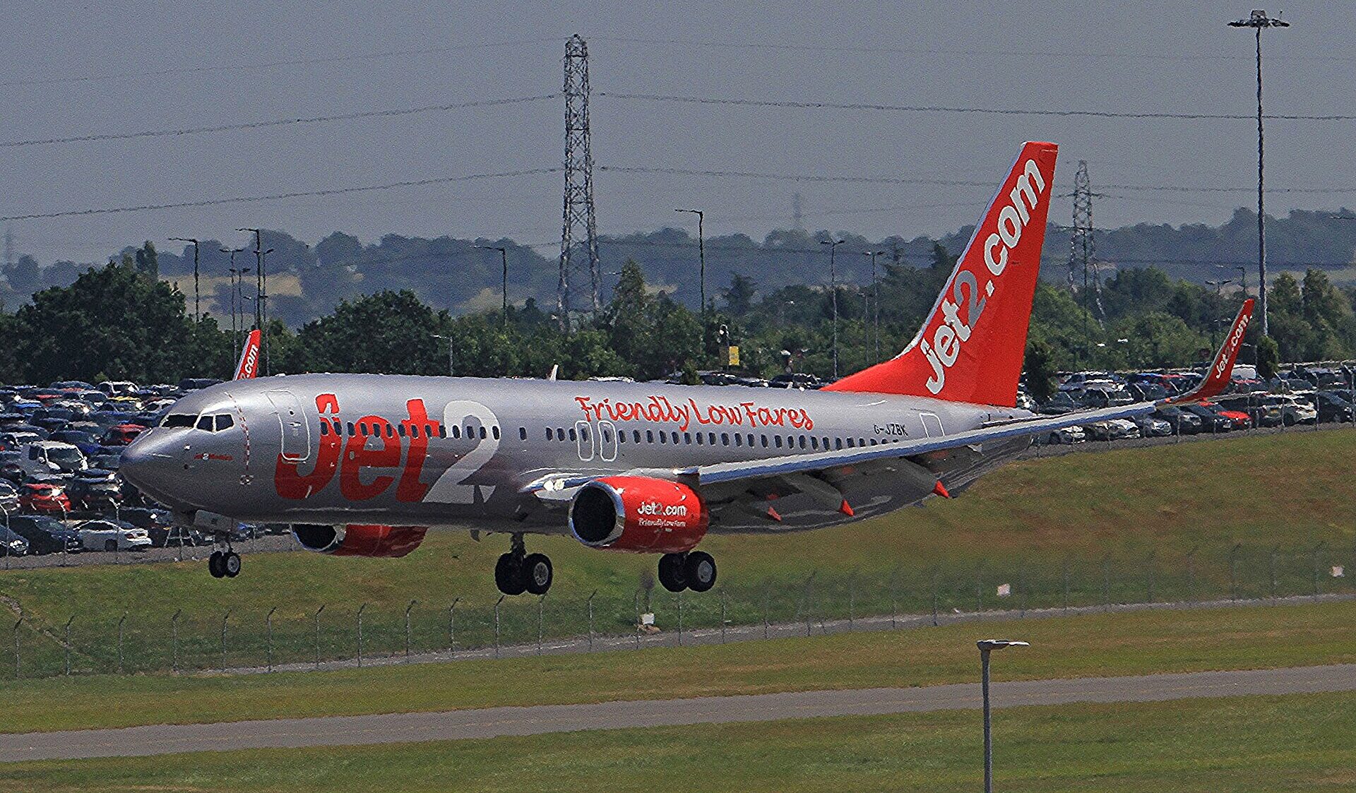 Jet2 Boeing aircraft takingoff on Birmingham runway. Trees and a car park in the background. Grey-ish sky in the background.