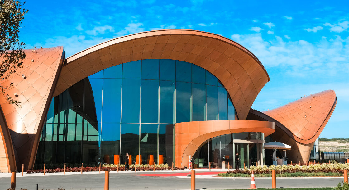 Jetex new terminal at Istanbul Airport. Cones in the foreground, blue sky with clouds in the background. Tall, glass windows with a brown dome-like building arch.