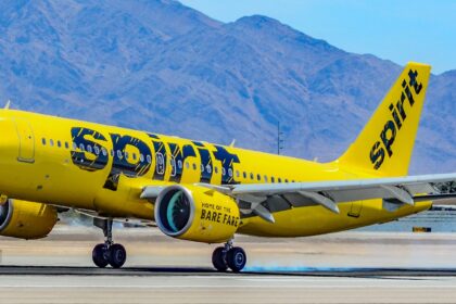 Spirit Airlines Airbus on the tarmac before takeoff. Yellow and black livery, in front of a blue sky with mountains in the background.