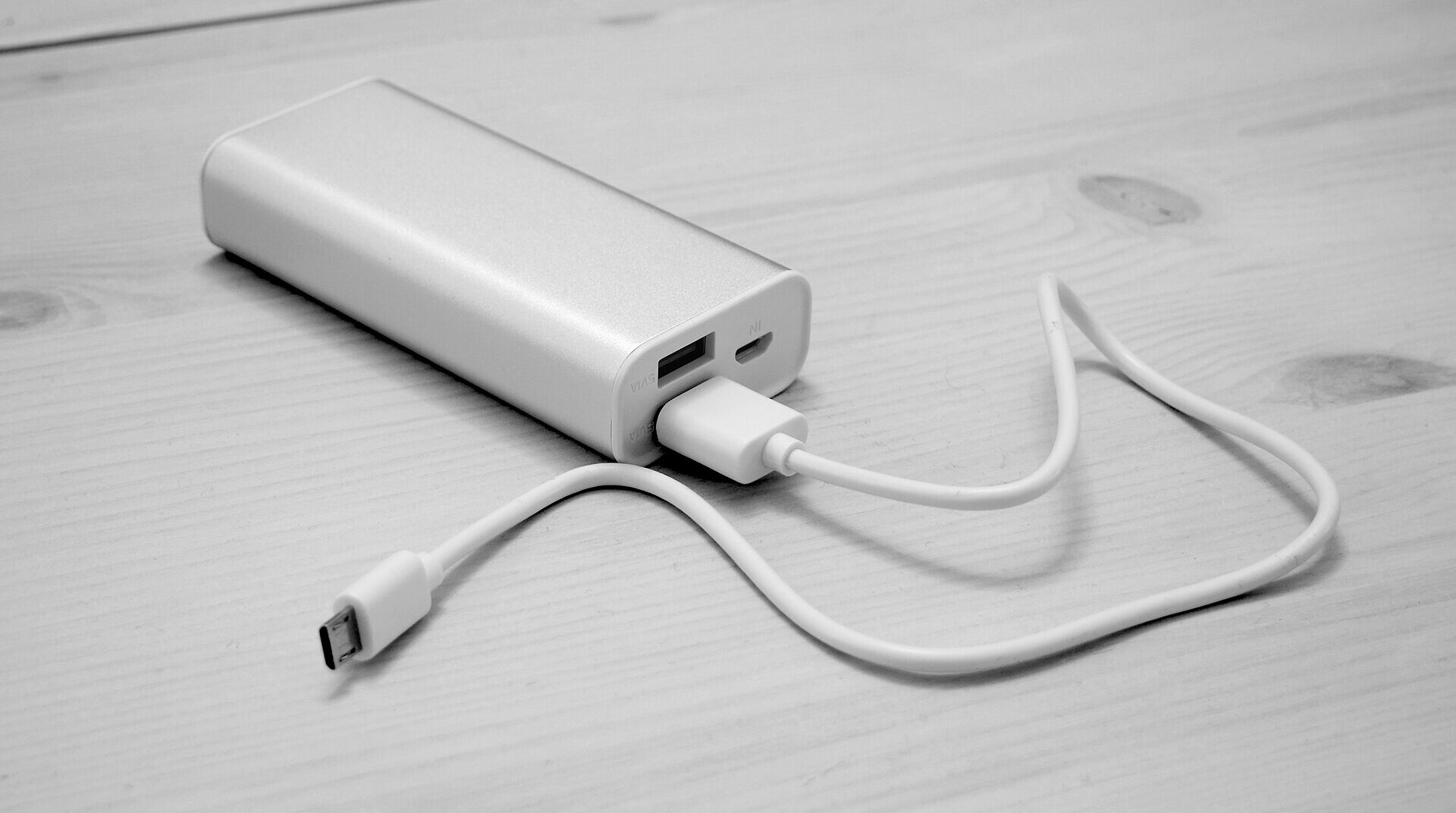 A white portable power bank with a cable attached to it, sitting on a white wooden table.