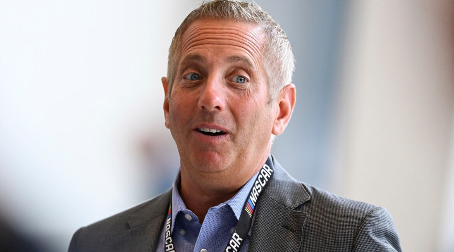 A man with grey hair wearing a suit and tie with a NASCAR lanyard around his neck
