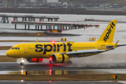 A large yellow Spirit Airlines jetliner on the runway beside a body of water