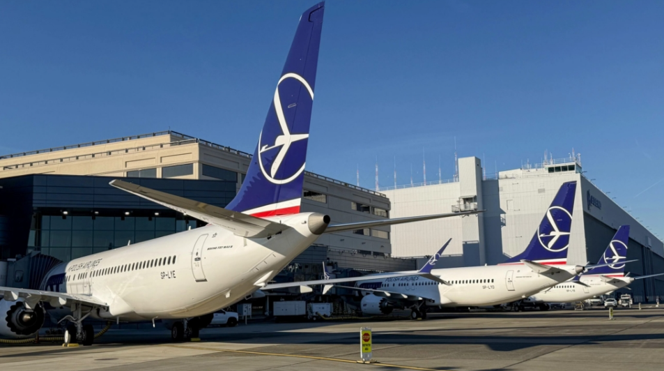 Blue and white jetliners sitting outside an airport below a blue sky. White buildings seen in the background.