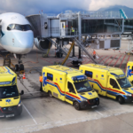 A large white jetliner sitting on a runway with four ambulances in front of it