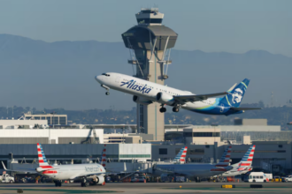 A white and blue plane taking off from a runway with an air traffic control tower