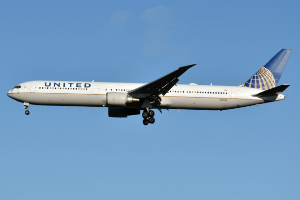 A United Airlines aircraft mid flight. the plane is white with the multi-coloured logo on the tail of the plane, which is on the centre right, and 'United' on the side of the aircraft close to the nose, which is on the centre left. The background is a clear pale blue sky.