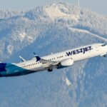 On a background of snowy mountains, a WestJet aircraft takes off into the sky,