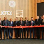 Jetex-Istanbul collaboration, colleagues standing in a line holding up a long sash. Men in suits and two women in red airline attire.