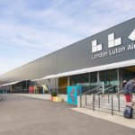 Outside of terminal at Luton Airport with the large airport sign that reads "LLA London Luton Airport".