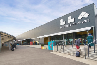 Outside of terminal at Luton Airport with the large airport sign that reads "LLA London Luton Airport".