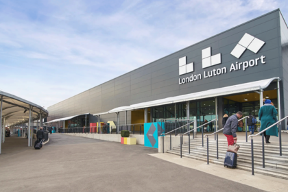 Outside of terminal at Luton Airport with the large airport sign that reads "LLA London Luton Airport".