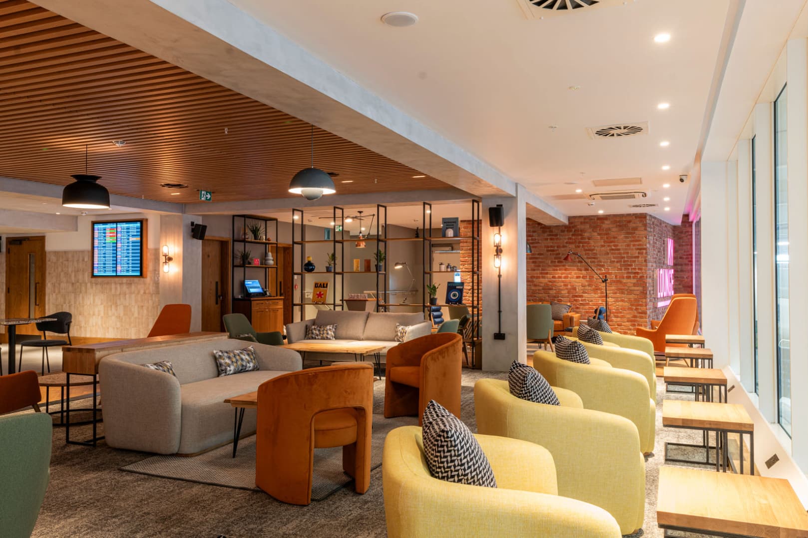LLA assisted travel lounge for passengers with reduced mobility or additional needs. Orange and yellow couch seats, with coffee tables.