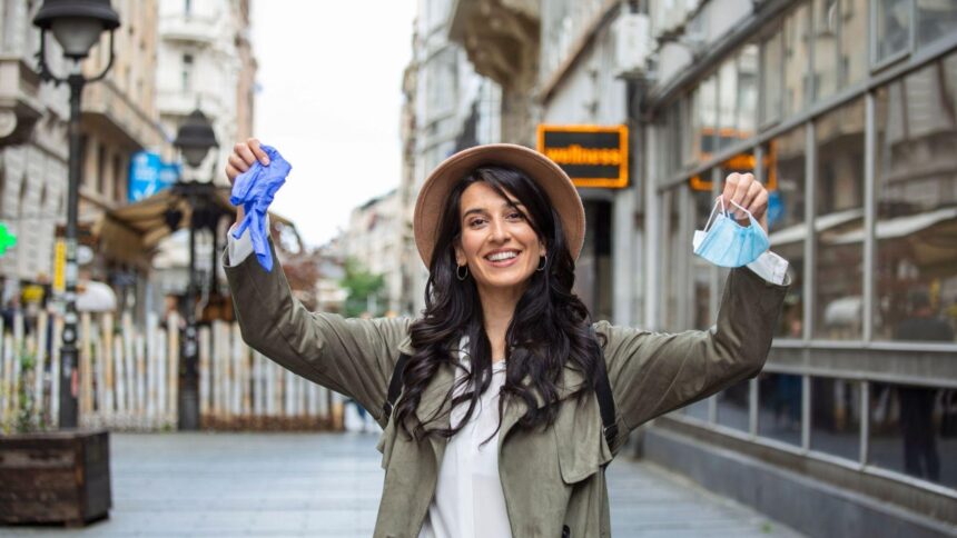 A traveller holding a used face mask and gloves in her hands in a town