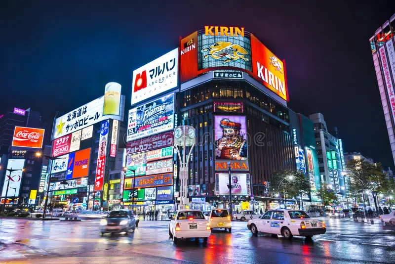 Night time in Sapporo. Corner of a street intersection with tall building covered in bright advertisements