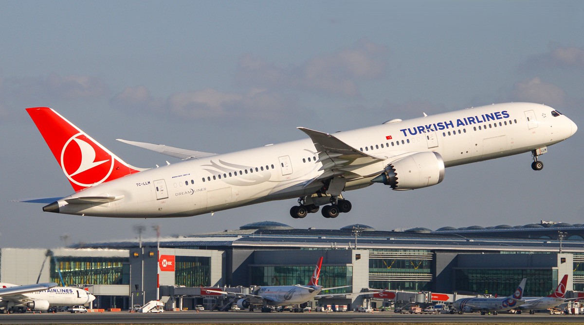 Turkish Airlines Boeing 787-9 Dreamliner TC-LLM taking off with Istanbul Airport terminal visible in the background.