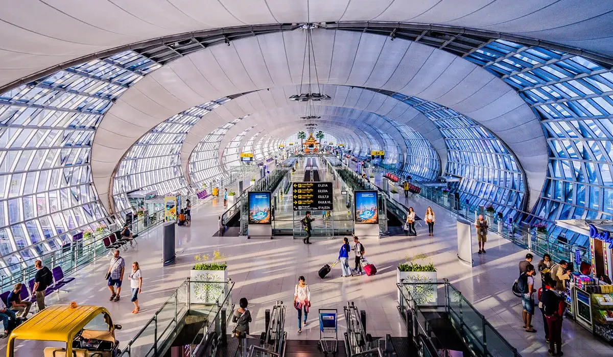 Chennai International Airport interior. Glass dome windows, travellers with suitcases. Escalators and departure signs in the background.