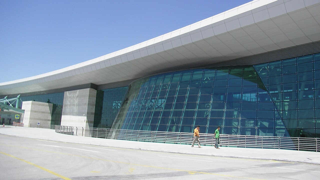 Image shows the outside of Ankara Airport terminal building during the day with two people walking