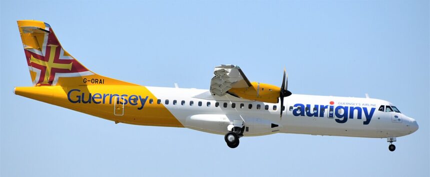 An Aurigny ATR 72-600 flying under a light blue sky. The aircraft is mostly white, however its tail is yellow and the logo is blue.