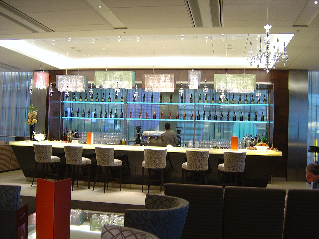 Luxury airline first-class suite featuring a spacious leather seat, fine dining table setup, personal minibar, large entertainment screen, and premium cabin finishes aboard an Emirates aircraft.