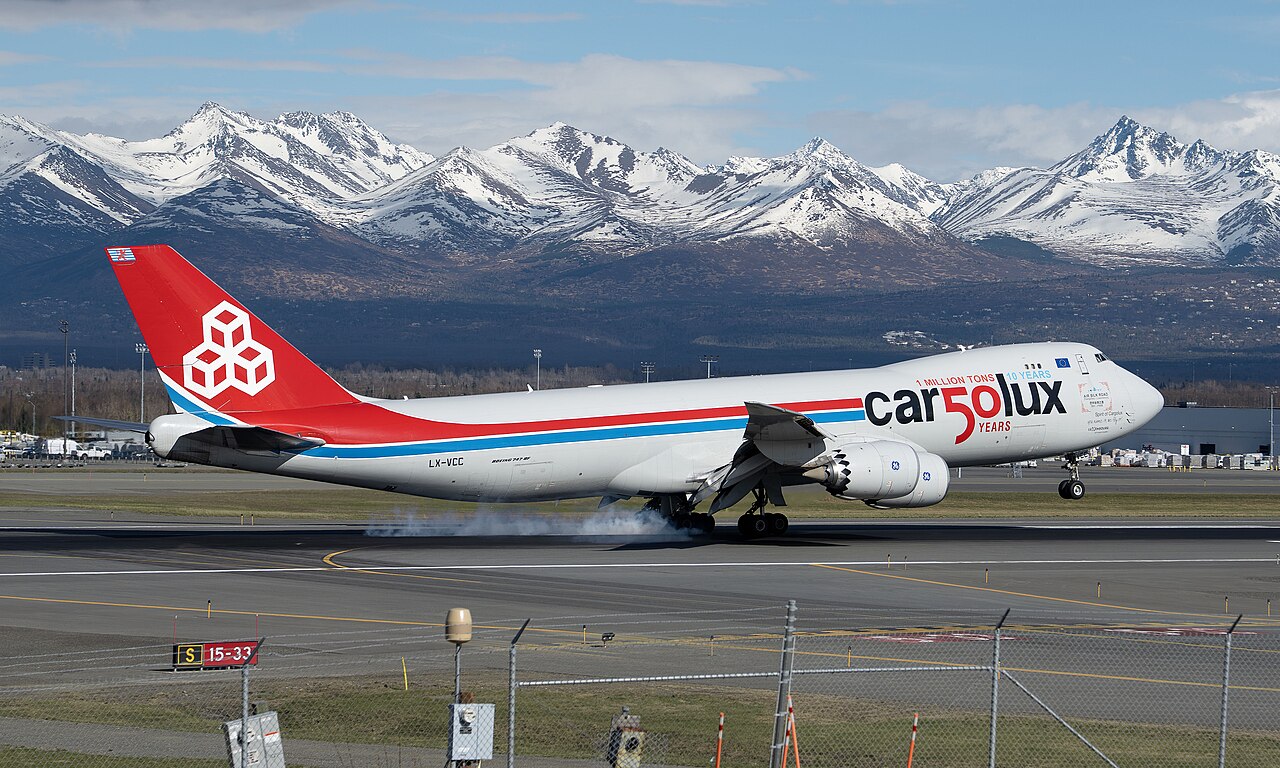 A Cargolux Boeing 747-8F (LX-VCC), on the runway in clear conditions with blue skies and snowy mountains as the backdrop.