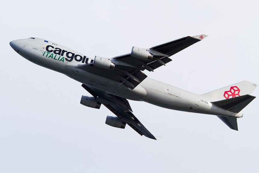Cargolux Italia Boeing 747 freighter in flight during climb-out, captured against a pale overcast sky. The aircraft is shown banking slightly upward with landing gear still extended, highlighting the aircraft shortly after takeoff.