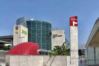 Outside view of Lisbon Airport's terminal one. The building is a mixture of light grey with a big glass wall. The sky is blue and red tube sines can also be seen