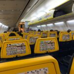 Interior of Ryain 737, with rows of yellow seat visible overhead light and cabin bag storage.