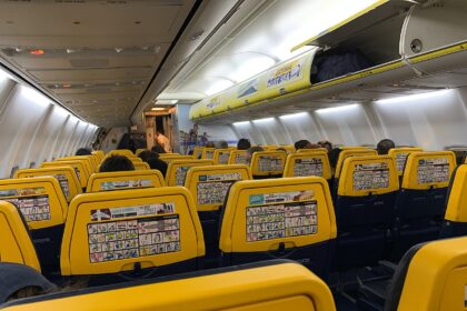 Interior of Ryain 737, with rows of yellow seat visible overhead light and cabin bag storage.
