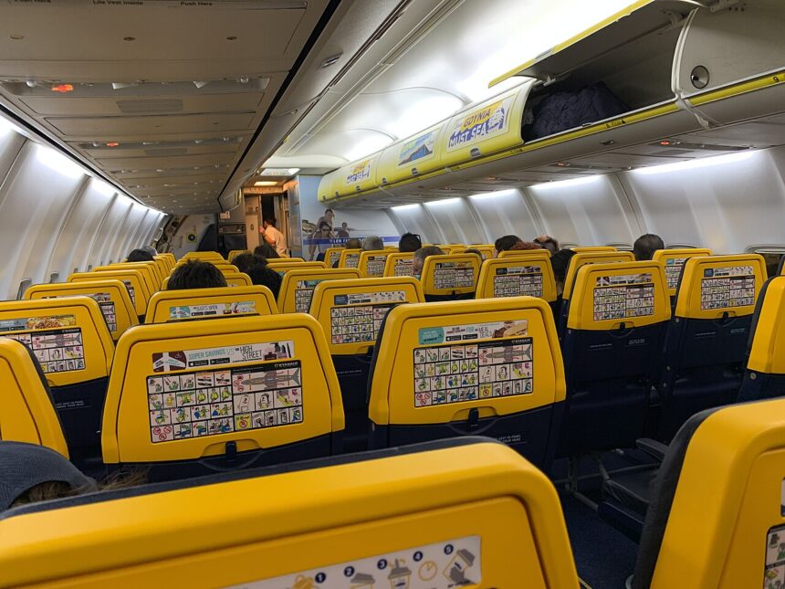 Interior of Ryain 737, with rows of yellow seat visible overhead light and cabin bag storage.