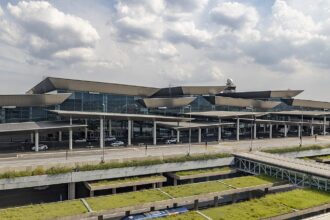 The outside of São Paulo International Airport (GRU) terminal 3, the international departure terminal. The sky is cloudy and the building is mostly grey but covered by windows.