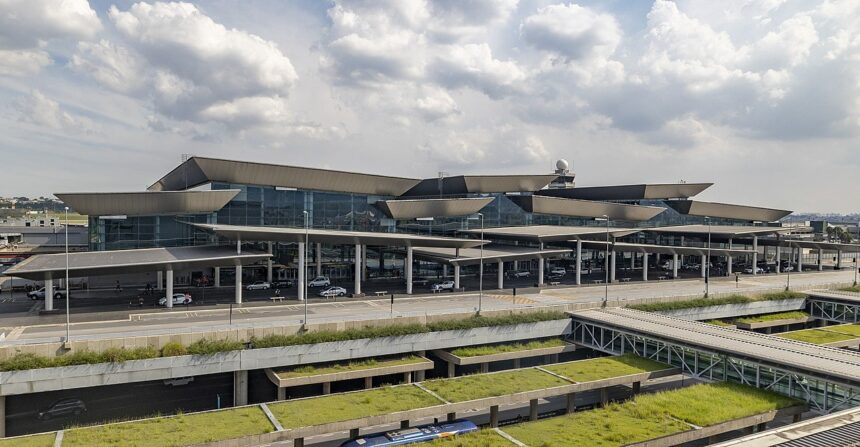 The outside of São Paulo International Airport (GRU) terminal 3, the international departure terminal. The sky is cloudy and the building is mostly grey but covered by windows.