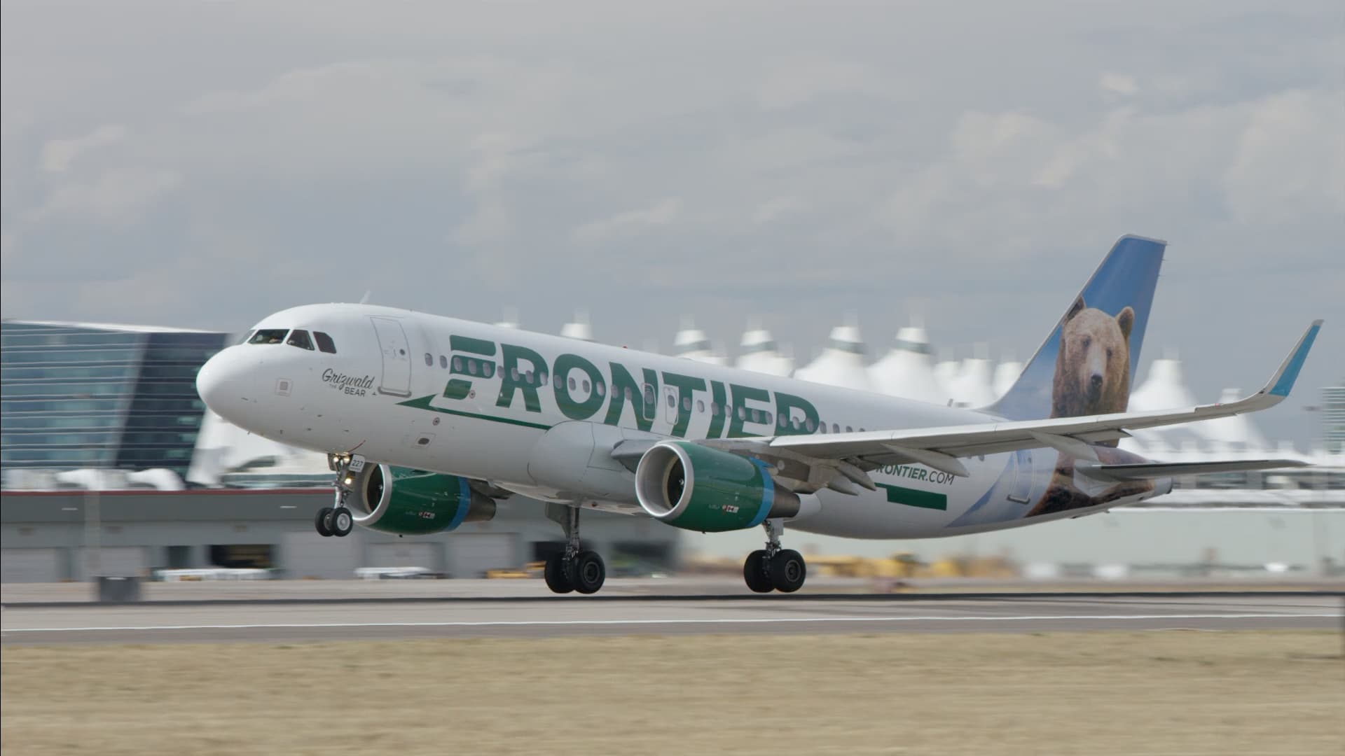 Frontier aircraft lifting off from the runway from a side view with a bear painting on the tail.