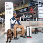 A man and his brown dog sit at the Air Canada accessibility entrance with a suitcase