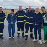 The band, Take That, with airport staff at Coventry Airport, outside. The black helicopter still visible in the background.