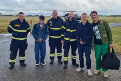 The band, Take That, with airport staff at Coventry Airport, outside. The black helicopter still visible in the background.