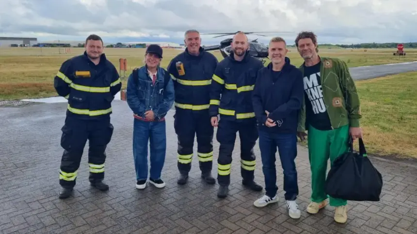 The band, Take That, with airport staff at Coventry Airport, outside. The black helicopter still visible in the background.