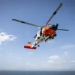 A white and orange U.S. Coast Guard MH-60 Jayhawk helicopter flying above water during a search and rescue training exercise.