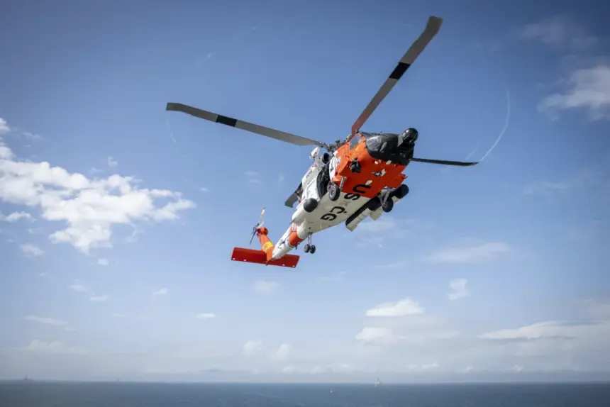 A white and orange U.S. Coast Guard MH-60 Jayhawk helicopter flying above water during a search and rescue training exercise.