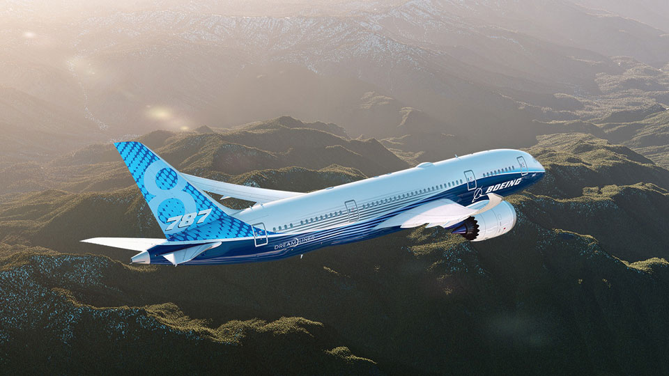 Boeing 787 Dreamliner in Boeing colours in flight above mountains and hills.